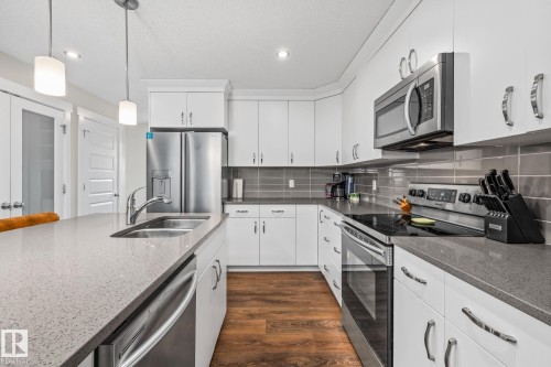 Kitchen featuring stainless steel appliances, dark wood-type flooring, dark stone counters, decorative light fixtures, and a textured ceiling - 1315 Chappelle Boulevard, Edmonton, AB - Indoor Photo Showing Kitchen With Double Sink With Upgraded Kitchen