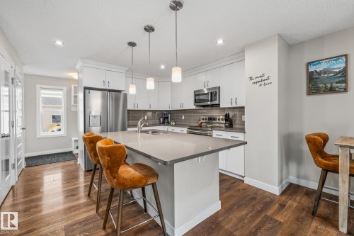 Kitchen featuring white cabinets, a breakfast bar area, stainless steel appliances, a center island with sink, and dark wood finished floors - 1315 Chappelle Boulevard, Edmonton, AB - Indoor Photo Showing Kitchen With Upgraded Kitchen
