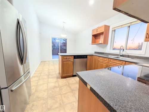 Kitchen featuring stainless steel appliances, dark countertops, lofted ceiling, a peninsula, and pendant lighting - 3307 24 Avenue, Edmonton, AB - Indoor Photo Showing Kitchen With Double Sink