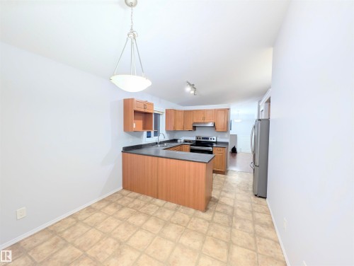 Kitchen featuring dark countertops, a peninsula, stainless steel appliances, wood finish cabinets, and hanging light fixtures - 3307 24 Avenue, Edmonton, AB - Indoor Photo Showing Kitchen