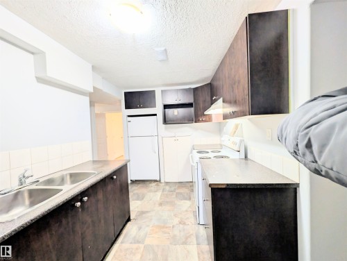Kitchen with dark wood finish cabinets, white appliances, a textured ceiling, and light countertops - 3307 24 Avenue, Edmonton, AB - Indoor Photo Showing Kitchen With Double Sink