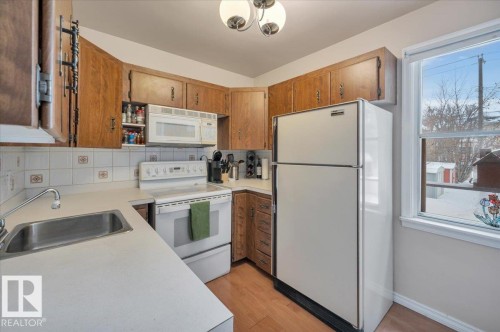 Kitchen with white appliances, light countertops, backsplash, wood finish cabinetry, and light wood-style floors - 7934 81 Avenue Nw, Edmonton, AB - Indoor Photo Showing Kitchen