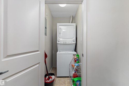 Laundry area featuring a textured ceiling, stacked washer / drying machine, and light tile patterned flooring - 231 344 Windermere Road, Edmonton, AB - Indoor Photo Showing Laundry Room