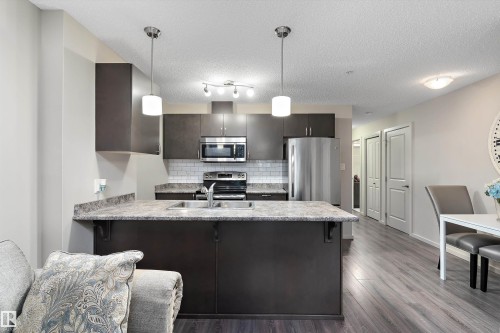 Kitchen featuring a peninsula, stainless steel appliances, decorative backsplash, dark wood finish cabinets, and dark wood-style floors - 231 344 Windermere Road, Edmonton, AB - Indoor Photo Showing Kitchen With Double Sink With Upgraded Kitchen
