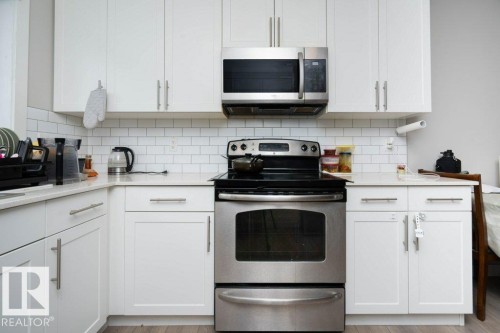 Kitchen with stainless steel appliances, white cabinetry, light stone countertops, and light wood finished floors - 96 1530 Tamarack Boulevard, Edmonton, AB - Indoor Photo Showing Kitchen With Upgraded Kitchen