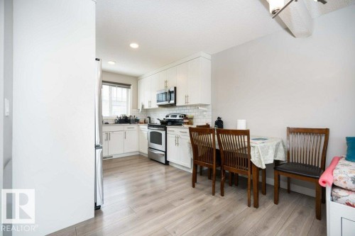 Kitchen featuring stainless steel appliances, white cabinets, light wood-style flooring, tasteful backsplash, and light countertops - 96 1530 Tamarack Boulevard, Edmonton, AB - Indoor