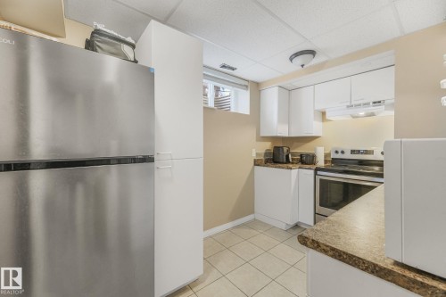 Kitchen featuring stainless steel appliances, dark countertops, a drop ceiling, white cabinets, and light tile patterned flooring - 2 Scarboro Place, St. Albert, AB - Indoor Photo Showing Kitchen