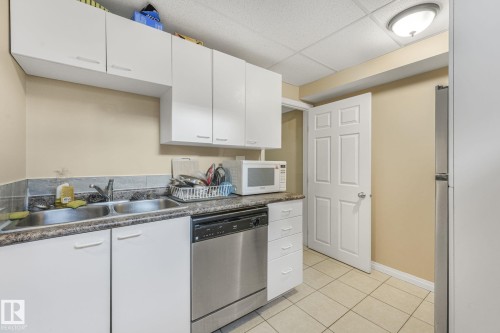 Kitchen with a paneled ceiling, stainless steel dishwasher, white cabinetry, dark countertops, and white microwave - 2 Scarboro Place, St. Albert, AB - Indoor Photo Showing Kitchen With Double Sink
