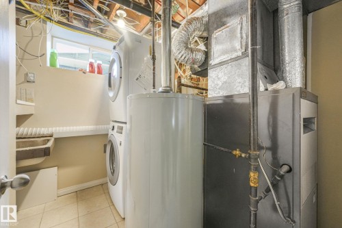 Laundry area with stacked washer and clothes dryer, water heater, heating unit, and light tile patterned floors - 2 Scarboro Place, St. Albert, AB - Indoor