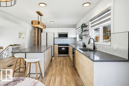 Kitchen featuring a breakfast bar area, dark stone counters, backsplash, decorative light fixtures, and white cabinetry - 7016 92A Avenue, Edmonton, AB - Indoor Photo Showing Kitchen With Upgraded Kitchen