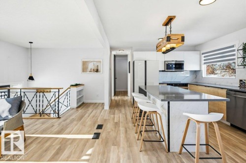 Kitchen with hanging light fixtures, stainless steel appliances, a kitchen breakfast bar, tasteful backsplash, and light wood finished floors - 7016 92A Avenue, Edmonton, AB - Indoor