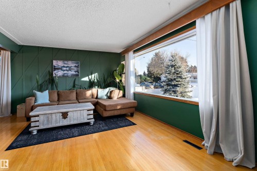 Living area featuring light wood finished floors, an accent wall, a textured ceiling, and a decorative wall - 7316 100 Avenue, Edmonton, AB - Indoor Photo Showing Other Room