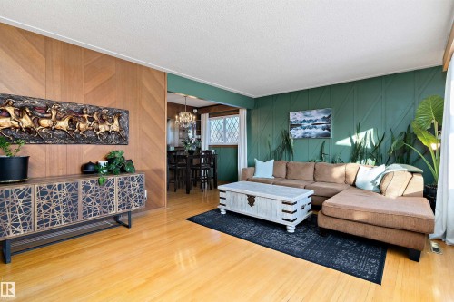 Living area featuring suspended lighting, a textured ceiling, light wood-type flooring, wooden walls, and ornamental molding - 7316 100 Avenue, Edmonton, AB - Indoor Photo Showing Living Room
