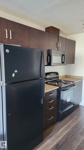 Kitchen with black appliances, a textured ceiling, dark wood-style floors, dark wood finish cabinets, and modern cabinets - 413 5521 7 Avenue, Edmonton, AB - Indoor Photo Showing Kitchen