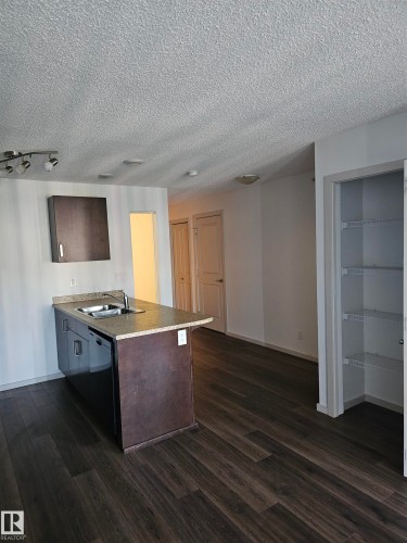 Kitchen with a peninsula, dark wood finish cabinets, light countertops, dark wood-style flooring, and a textured ceiling - 413 5521 7 Avenue, Edmonton, AB - Indoor Photo Showing Kitchen With Double Sink