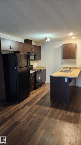 Kitchen featuring a peninsula, black appliances, dark wood-style flooring, a textured ceiling, and a kitchen bar - 413 5521 7 Avenue, Edmonton, AB - Indoor Photo Showing Kitchen