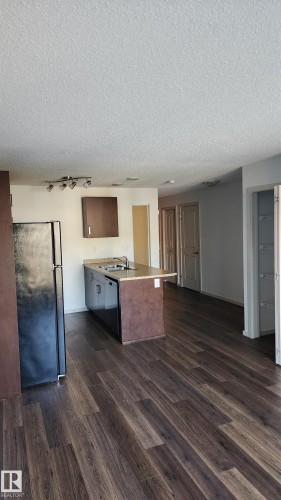 Kitchen featuring a peninsula, a textured ceiling, black appliances, light countertops, and dark wood-style floors - 413 5521 7 Avenue, Edmonton, AB - Indoor Photo Showing Kitchen