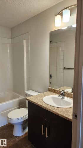 Full bathroom with vanity, shower / bathtub combination, a textured ceiling, and dark tile patterned floors - 413 5521 7 Avenue, Edmonton, AB - Indoor Photo Showing Bathroom