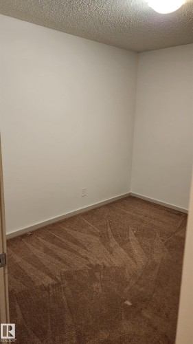 Unfurnished room featuring dark carpet and a textured ceiling - 413 5521 7 Avenue, Edmonton, AB - Indoor Photo Showing Other Room