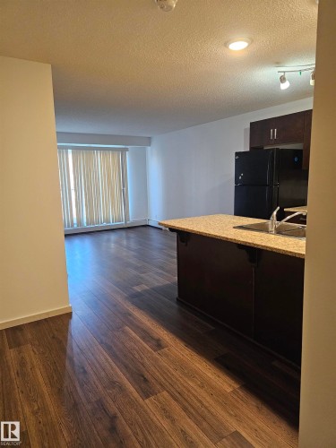 Kitchen with a kitchen bar, freestanding refrigerator, dark wood finish cabinets, dark wood finished floors, and a textured ceiling - 413 5521 7 Avenue, Edmonton, AB - Indoor