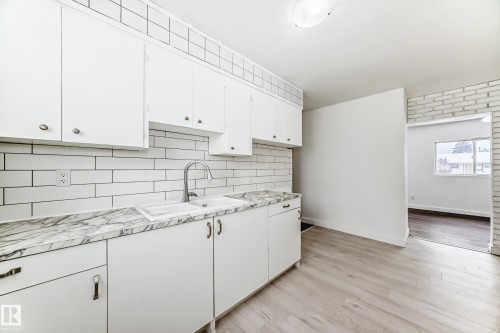 Kitchen featuring white cabinets, light countertops, decorative backsplash, and light wood-type flooring - 13904 135 Avenue, Edmonton, AB - Indoor Photo Showing Kitchen