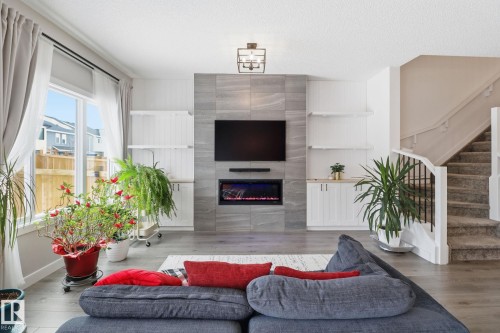 Living area featuring wood finished floors, a tile fireplace, a textured ceiling, and built in features - 3234 Chernowski Way, Edmonton, AB - Indoor Photo Showing Living Room With Fireplace