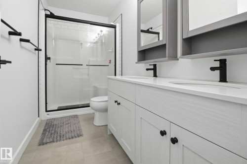 Full bath featuring double vanity, a shower stall, a textured ceiling, and light tile patterned flooring - 3234 Chernowski Way, Edmonton, AB - Indoor Photo Showing Bathroom