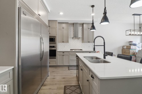 Kitchen featuring gray cabinetry, built in appliances, an island with sink, light wood finished floors, and decorative backsplash - 3234 Chernowski Way, Edmonton, AB - Indoor Photo Showing Kitchen With Stainless Steel Kitchen With Double Sink With Upgraded Kitchen