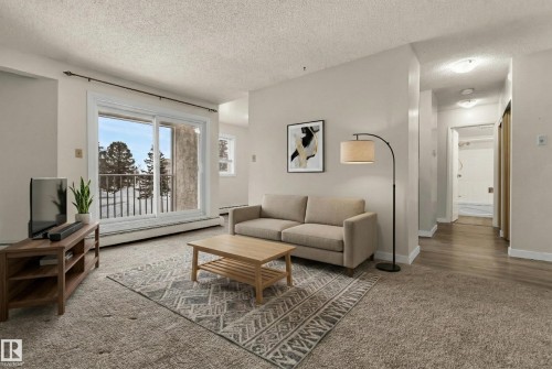 Living room with baseboard heating, carpet flooring, and a textured ceiling - 25 11255 31 Avenue, Edmonton, AB - Indoor Photo Showing Living Room