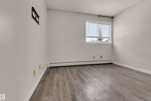 Empty room featuring light wood finished floors, baseboard heating, and a textured ceiling - 25 11255 31 Avenue, Edmonton, AB - Indoor Photo Showing Other Room