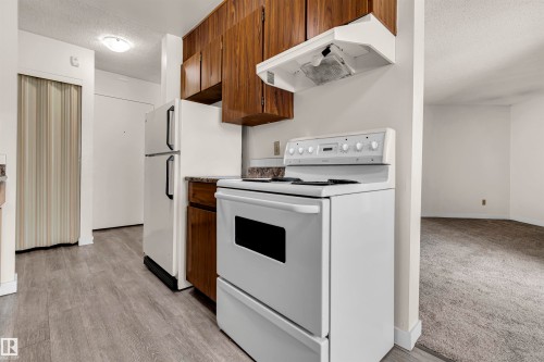 Kitchen featuring a textured ceiling, white range with electric cooktop, light countertops, and light wood-style flooring - 25 11255 31 Avenue, Edmonton, AB - Indoor Photo Showing Kitchen