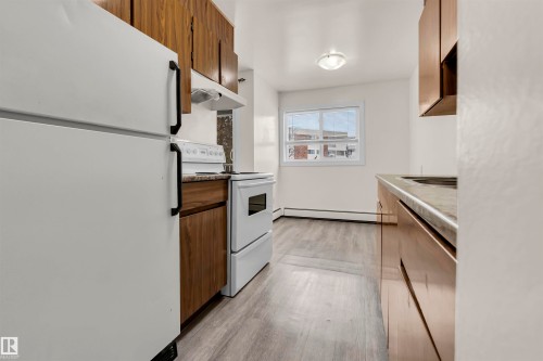 Kitchen featuring white appliances, light wood-type flooring, wood finish cabinetry, and a baseboard radiator - 25 11255 31 Avenue, Edmonton, AB - Indoor Photo Showing Kitchen