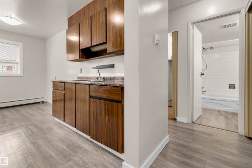 Kitchen with light wood-type flooring, baseboard heating, dark stone counters, and wood finish cabinets - 25 11255 31 Avenue, Edmonton, AB - Indoor