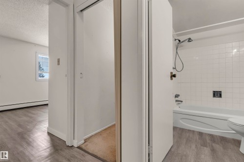 Bathroom with shower / tub combination, light wood-style floors, a textured ceiling, and baseboard heating - 25 11255 31 Avenue, Edmonton, AB - Indoor Photo Showing Bathroom