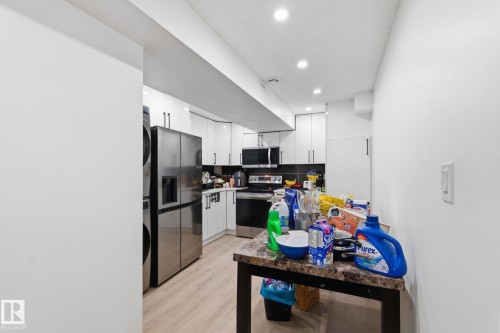 Kitchen with white cabinetry, stainless steel appliances, stacked washer / dryer, light wood-type flooring, and recessed lighting - 13538 127 Street, Edmonton, AB - Indoor