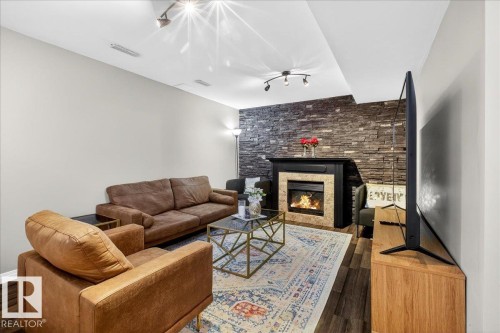 Area featuring a stone fireplace and dark wood-type flooring - 47 230 Edwards Drive, Edmonton, AB - Indoor Photo Showing Living Room With Fireplace