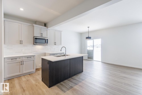 Dual tone kitchen with stainless steel microwave, a kitchen island with sink, light wood-style flooring, dual tone cabinetry, and tasteful backsplash - 75 Dansereau Way, Beaumont, AB - Indoor Photo Showing Kitchen