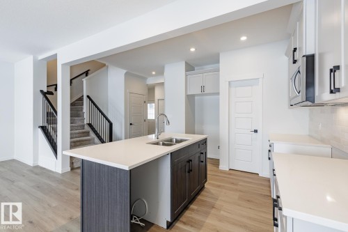 Kitchen featuring an island with sink, light wood finished floors, two tone cabinetry, light stone countertops, and stainless steel microwave - 75 Dansereau Way, Beaumont, AB - Indoor Photo Showing Kitchen With Double Sink