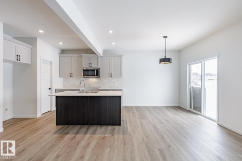 Kitchen featuring an island with sink, beamed ceiling, light wood-style floors, stainless steel microwave, and tasteful backsplash - 75 Dansereau Way, Beaumont, AB - Indoor Photo Showing Kitchen