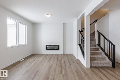 Unfurnished living room with light wood-style flooring and a glass covered fireplace - 75 Dansereau Way, Beaumont, AB - Indoor Photo Showing Other Room With Fireplace