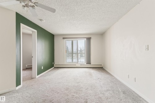Carpeted empty room with a textured ceiling, a baseboard radiator, and a ceiling fan - 312 11620 9A Avenue, Edmonton, AB - Indoor Photo Showing Other Room