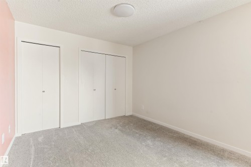 Unfurnished bedroom with carpet floors, a textured ceiling, and two closets - 312 11620 9A Avenue, Edmonton, AB - Indoor Photo Showing Other Room