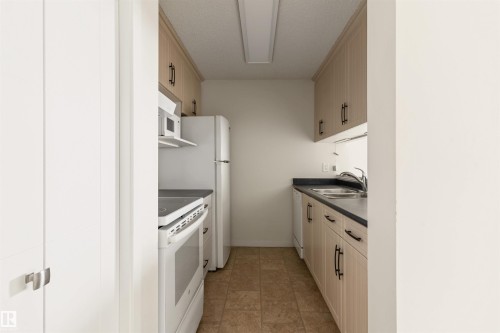 Kitchen featuring white appliances, dark countertops, and a textured ceiling - 312 11620 9A Avenue, Edmonton, AB - Indoor Photo Showing Kitchen With Double Sink
