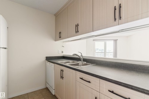 Kitchen featuring dark countertops, white appliances, light tile patterned floors, and arched walkways - 312 11620 9A Avenue, Edmonton, AB - Indoor Photo Showing Kitchen With Double Sink