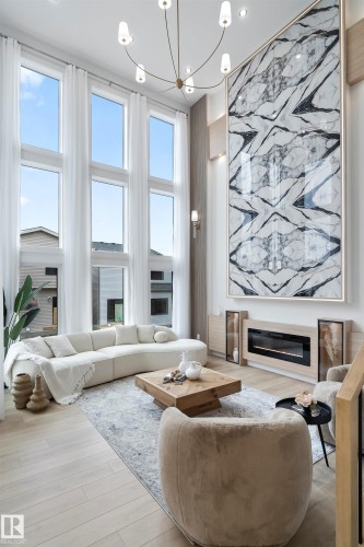 Living room with a glass covered fireplace, a high ceiling, light wood-style floors, and healthy amount of natural light - 7026 Kiviaq Crescent, Edmonton, AB - Indoor Photo Showing Living Room With Fireplace