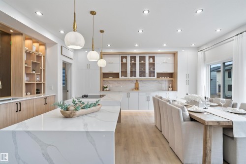 Kitchen featuring open shelves, light stone counters, a center island, light wood-style floors, and pendant lighting - 7026 Kiviaq Crescent, Edmonton, AB - Indoor Photo Showing Kitchen With Upgraded Kitchen
