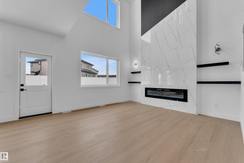 Unfurnished living room featuring a high ceiling, a tile fireplace, and light wood-style flooring - 741 Astoria Way, Devon, AB - Indoor With Fireplace
