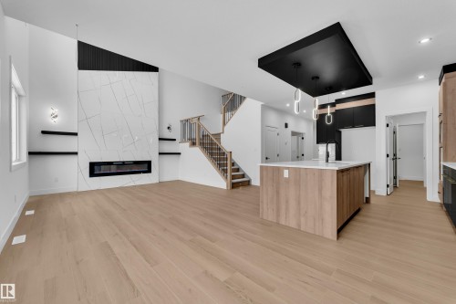 Kitchen with a center island with sink, open floor plan, a premium fireplace, light stone counters, and modern cabinets - 741 Astoria Way, Devon, AB - Indoor With Fireplace