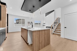 Kitchen featuring a center island with sink, hanging light fixtures, light stone countertops, light wood finished floors, and dual tone cabinetry - 