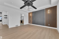 Unfurnished living room with a tray ceiling, ceiling fan, light wood-style floors, and an accent wall - 